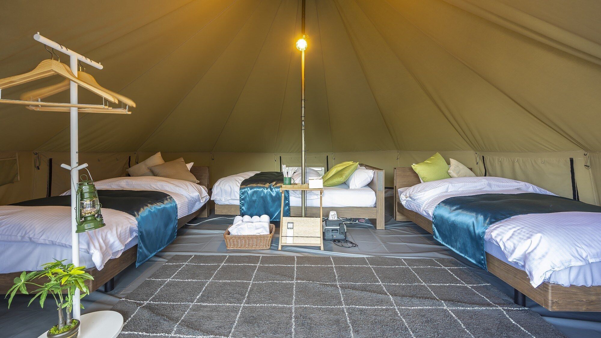 A tented accommodation with two beds, a hanging light, and a small table with a lamp.