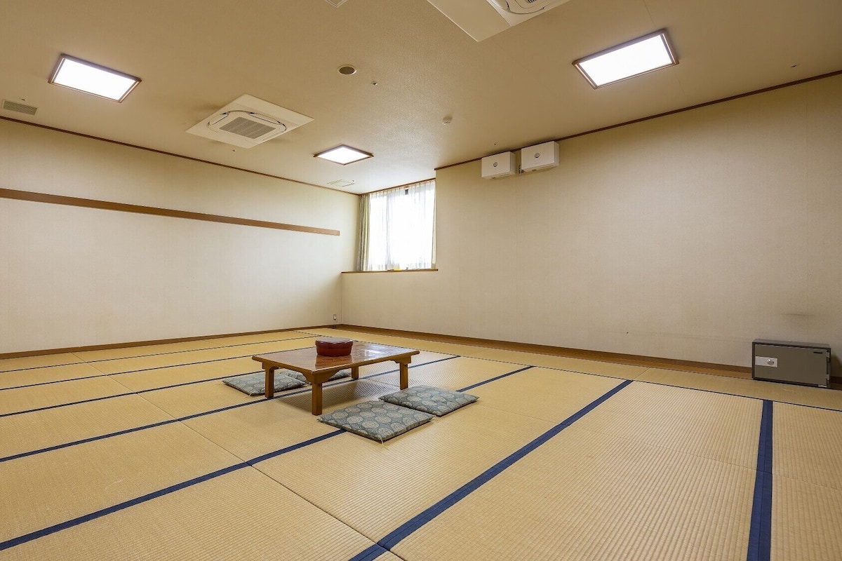A tatami mat room with a low table and cushions, ceiling lights, and a window.