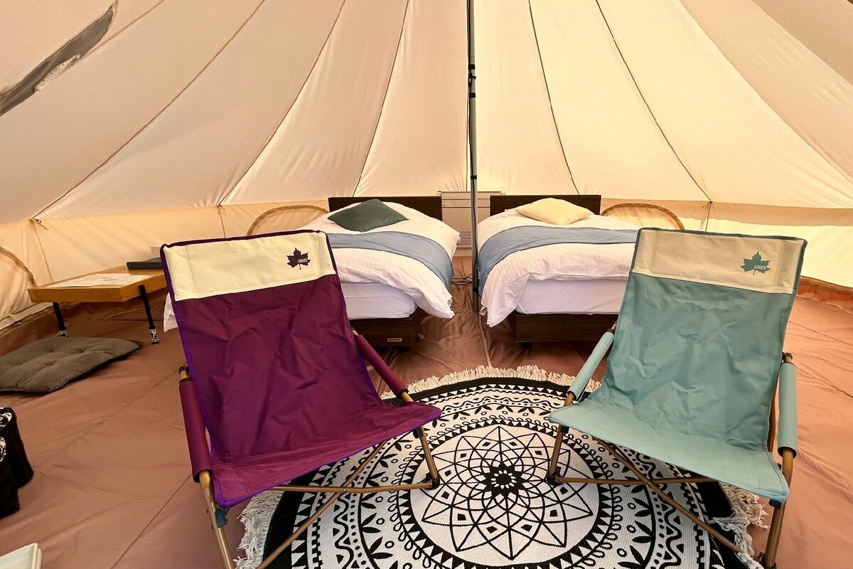 A tent with two beds, a patterned rug, and camping chairs.