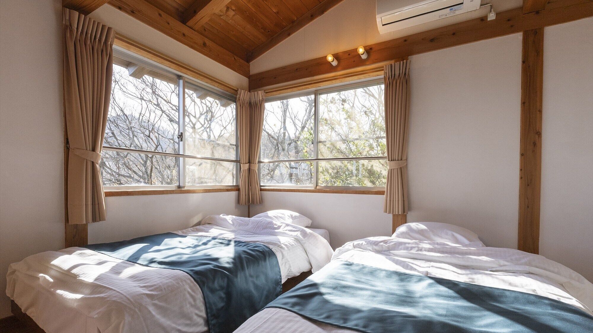 A room with two beds, wooden beams, large windows, and an air conditioning unit.