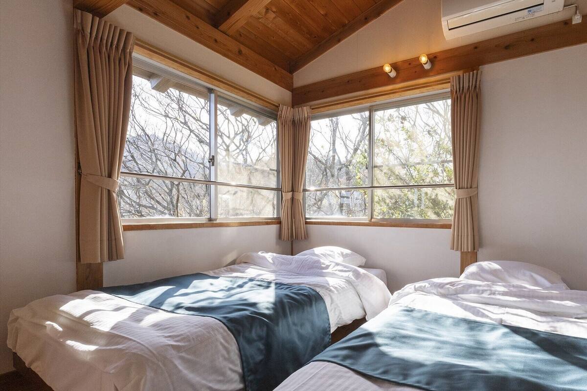 A room with two beds, wooden beams, large windows, and an air conditioning unit.