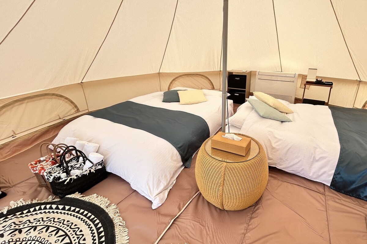 A tent with two beds, a wicker basket, and a small table with a lamp.