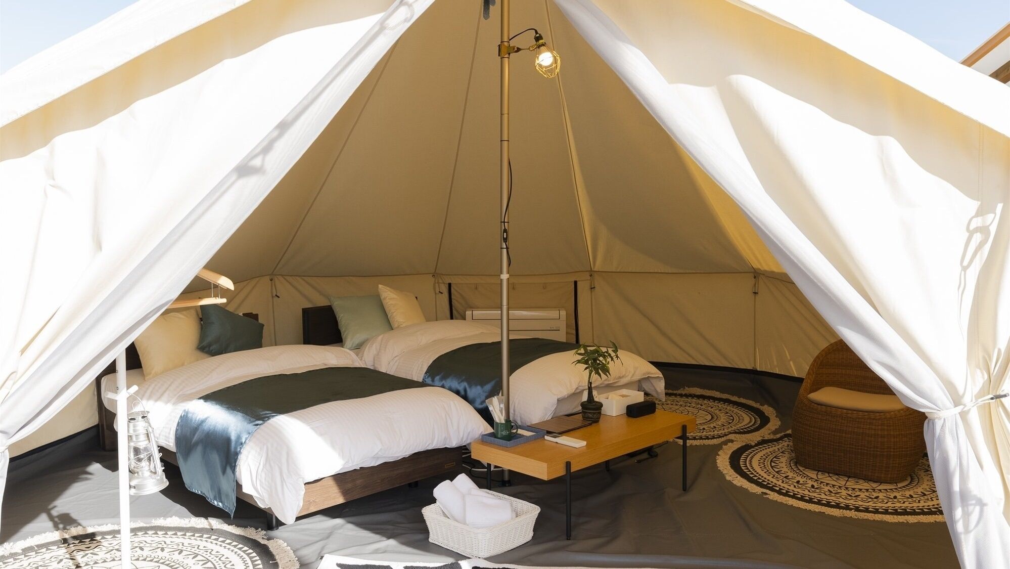 A tent with two beds, a bedside table, a lamp, a chair, and a patterned rug.