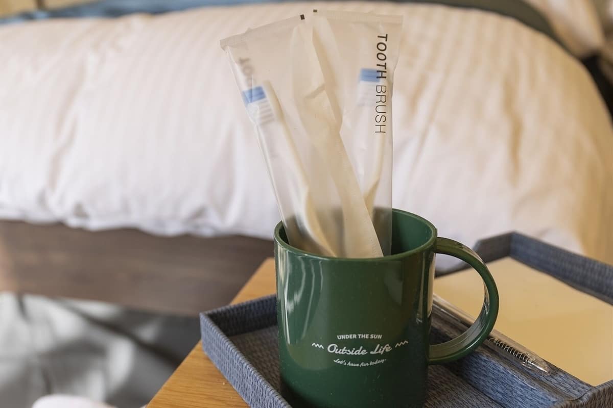 A green mug with a toothbrush and toothpaste on a tray in a hotel room.