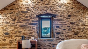 Una habitación con pared de piedra, ventana con vistas, escritorio con silla y sofá.