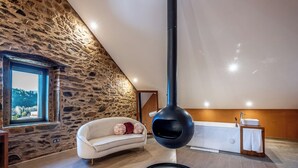 Una habitación con pared de piedra, un sofá blanco, una lámpara colgante negra y una bañera con una mesita de noche de madera.