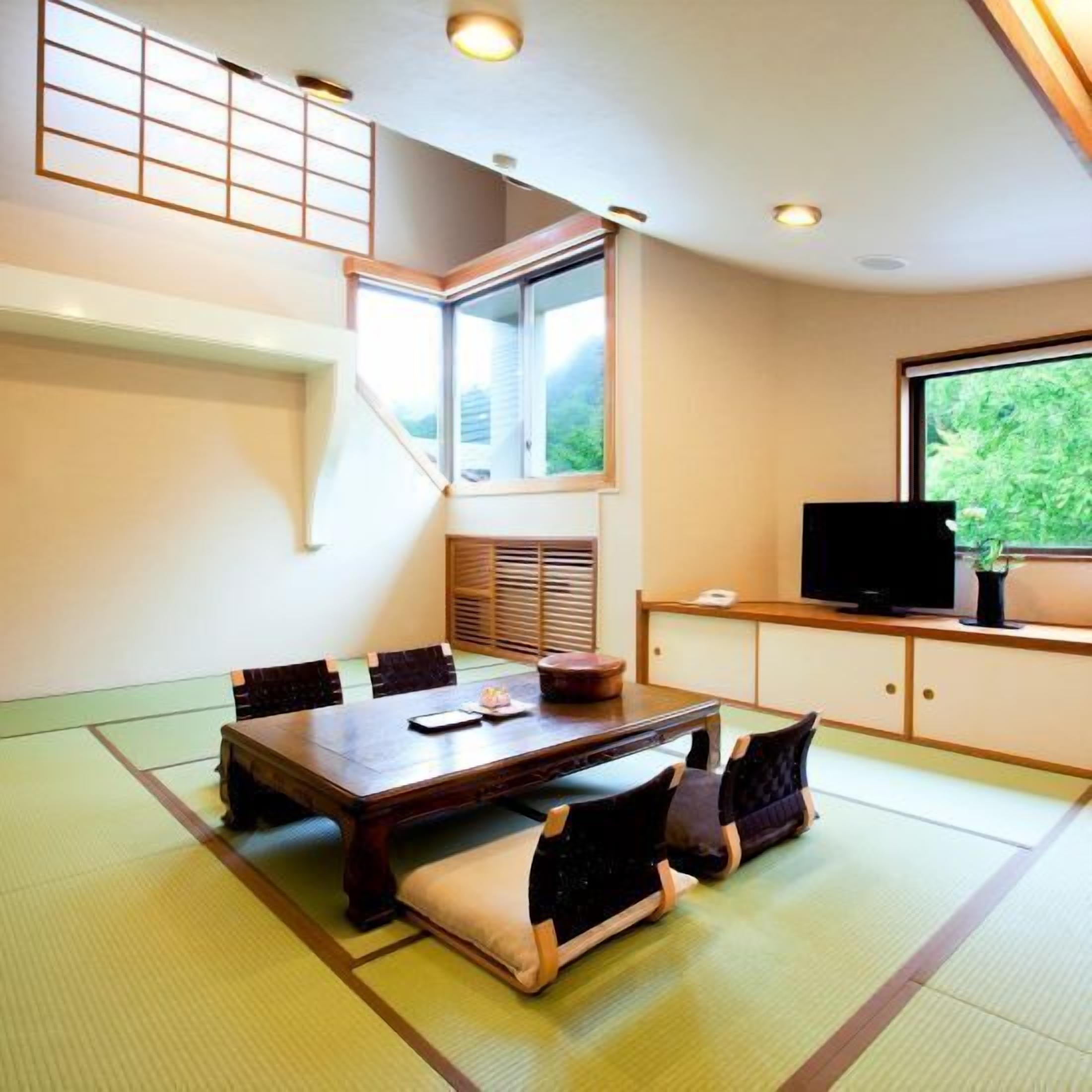 A traditional tatami mat room with a dining table, cushions, a TV, and a window with a view of greenery.
