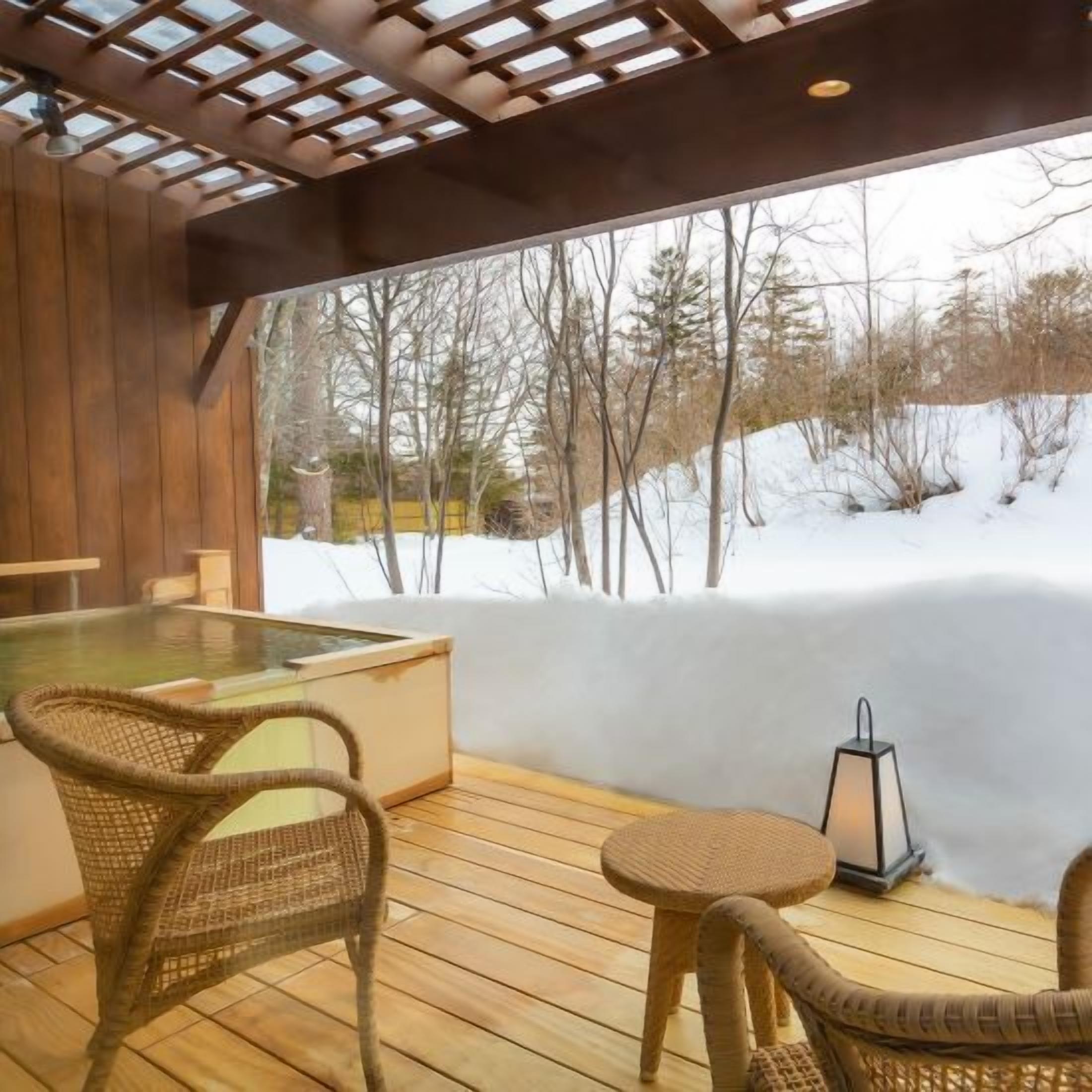 A wooden deck with a hot tub, wicker chairs, and a view of a snowy landscape.