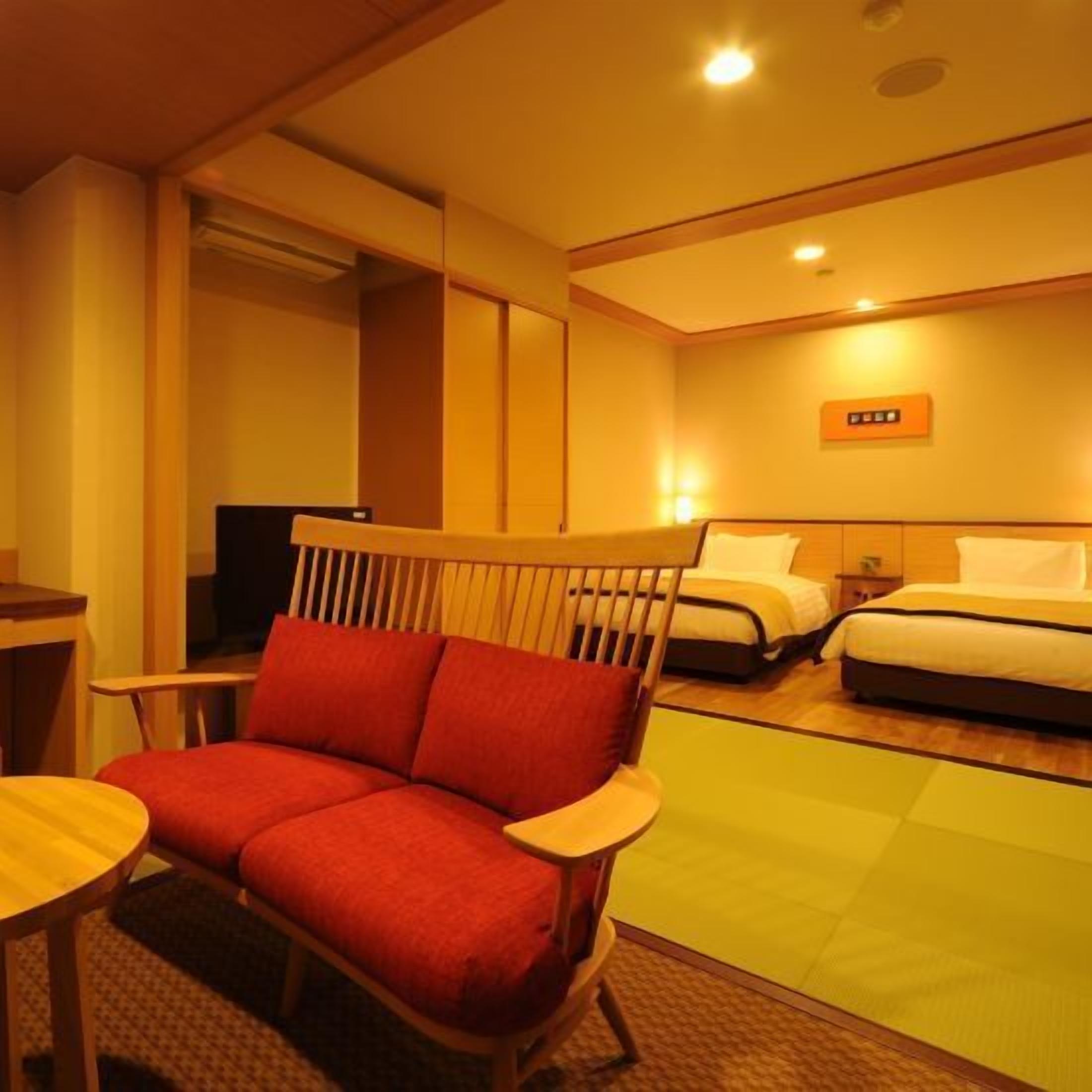 A hotel room with a wooden chair, two beds, a small table, and a wall-mounted control panel.
