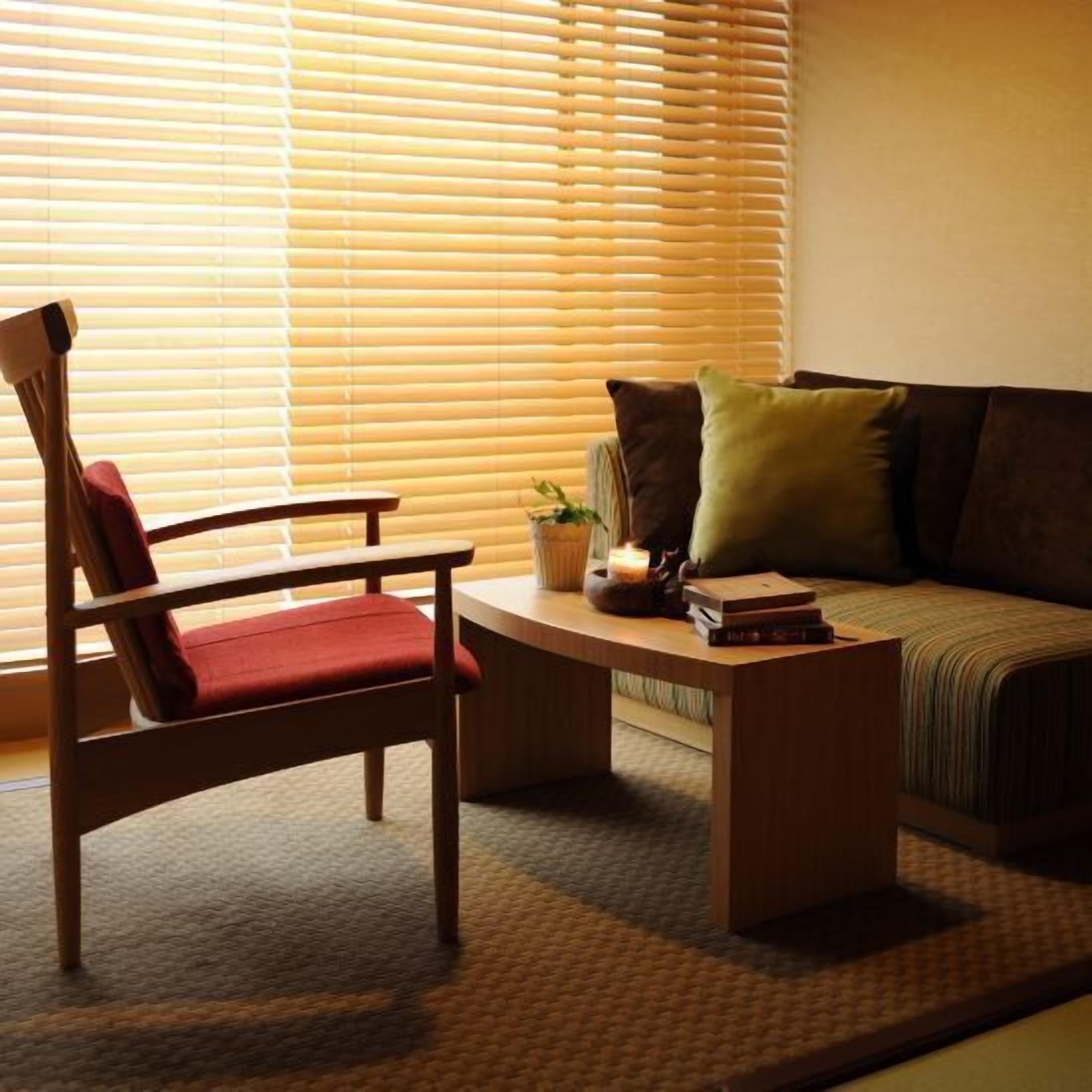 A room with a wooden chair, a sofa, a coffee table, and a window with blinds.