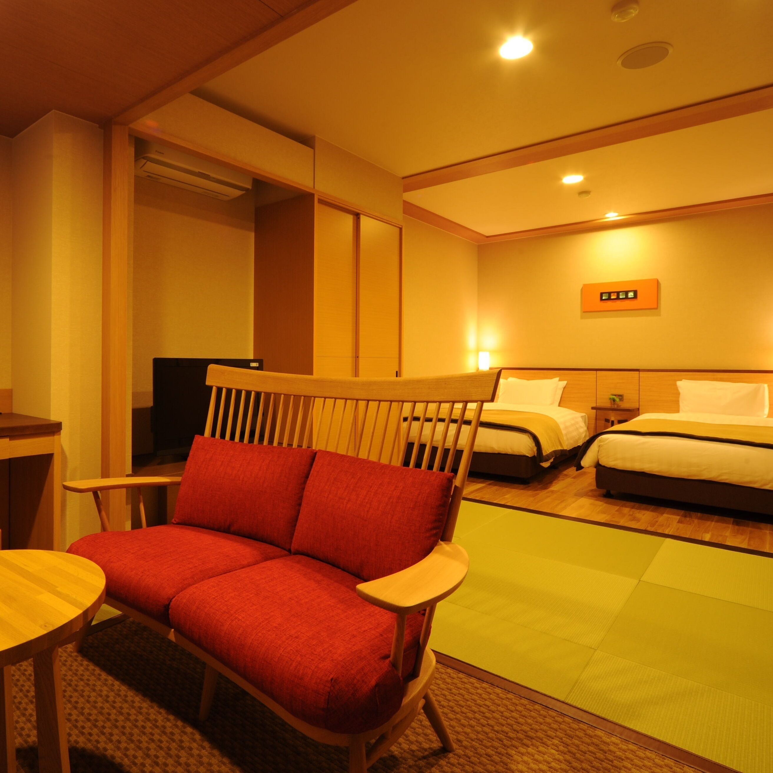 A hotel room with a sofa, two beds, a small table, and a mirror.