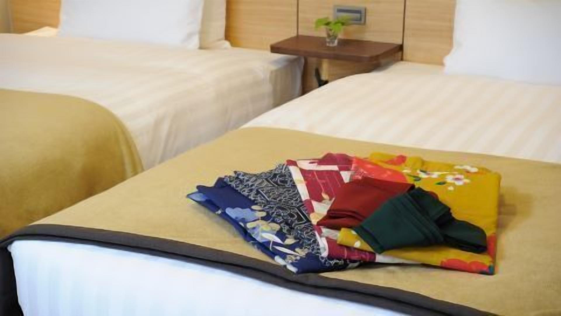 A hotel room with two beds, a small bedside table with a plant, and a neatly folded blanket on the bed.