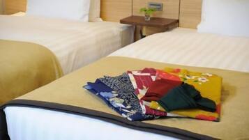 A hotel room with two beds, a small bedside table with a plant, and a neatly folded blanket on the bed.