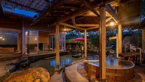 A traditional Japanese onsen with wooden architecture, a stone hot spring, and a red umbrella. - Fukujuso Onsen Ryokan (Shima)