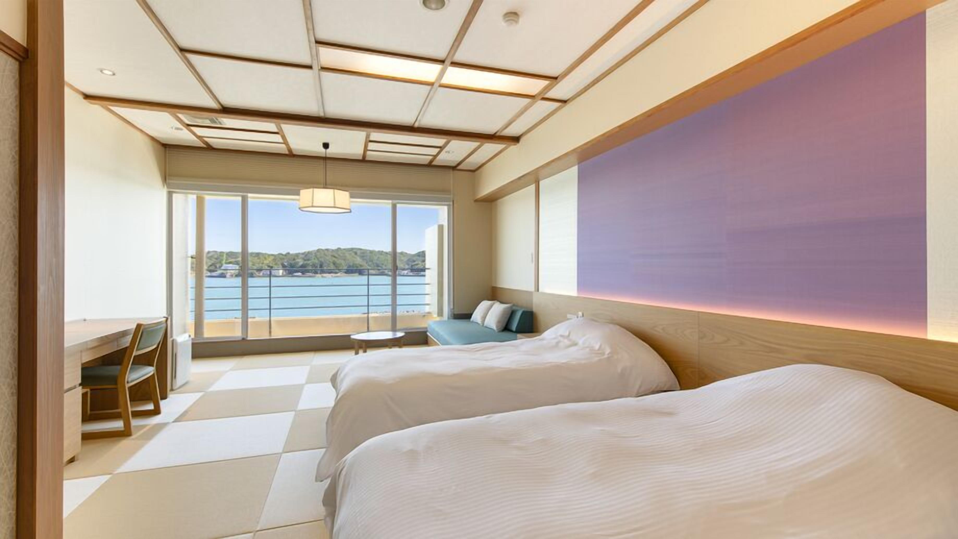 Habitació d'hotel amb dos llits, un escriptori, una cadira i vista al mar.