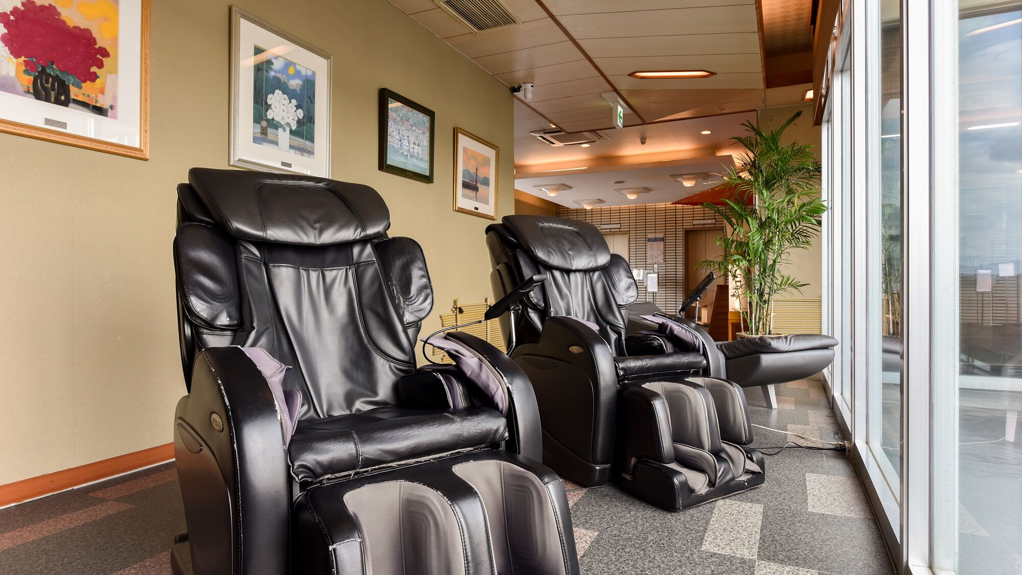 A massage therapy room with two massage chairs, a potted plant, and framed artwork on the wall.