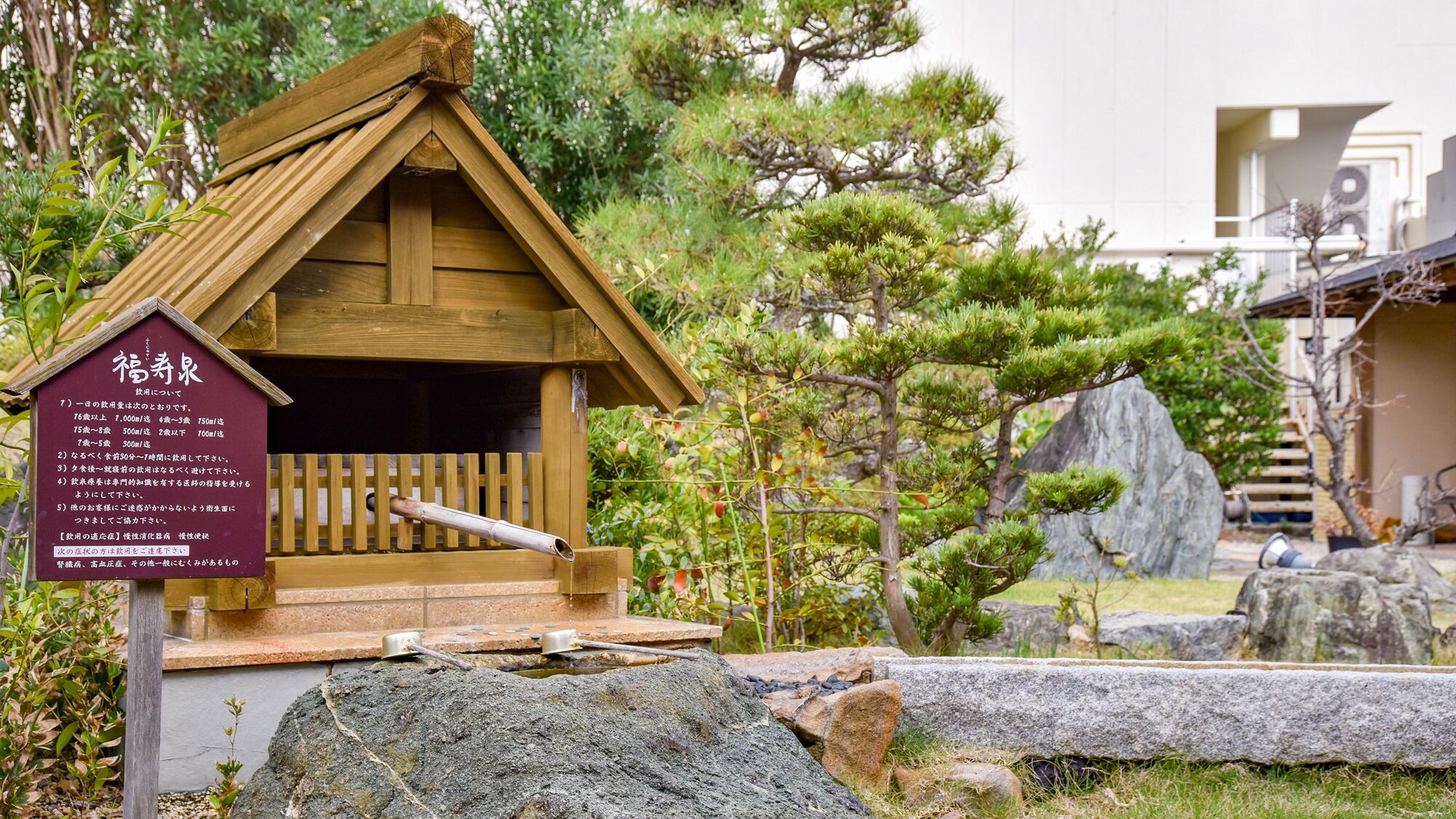 A wooden structure with a sloped roof, a sign with text, and a natural setting with rocks and trees.