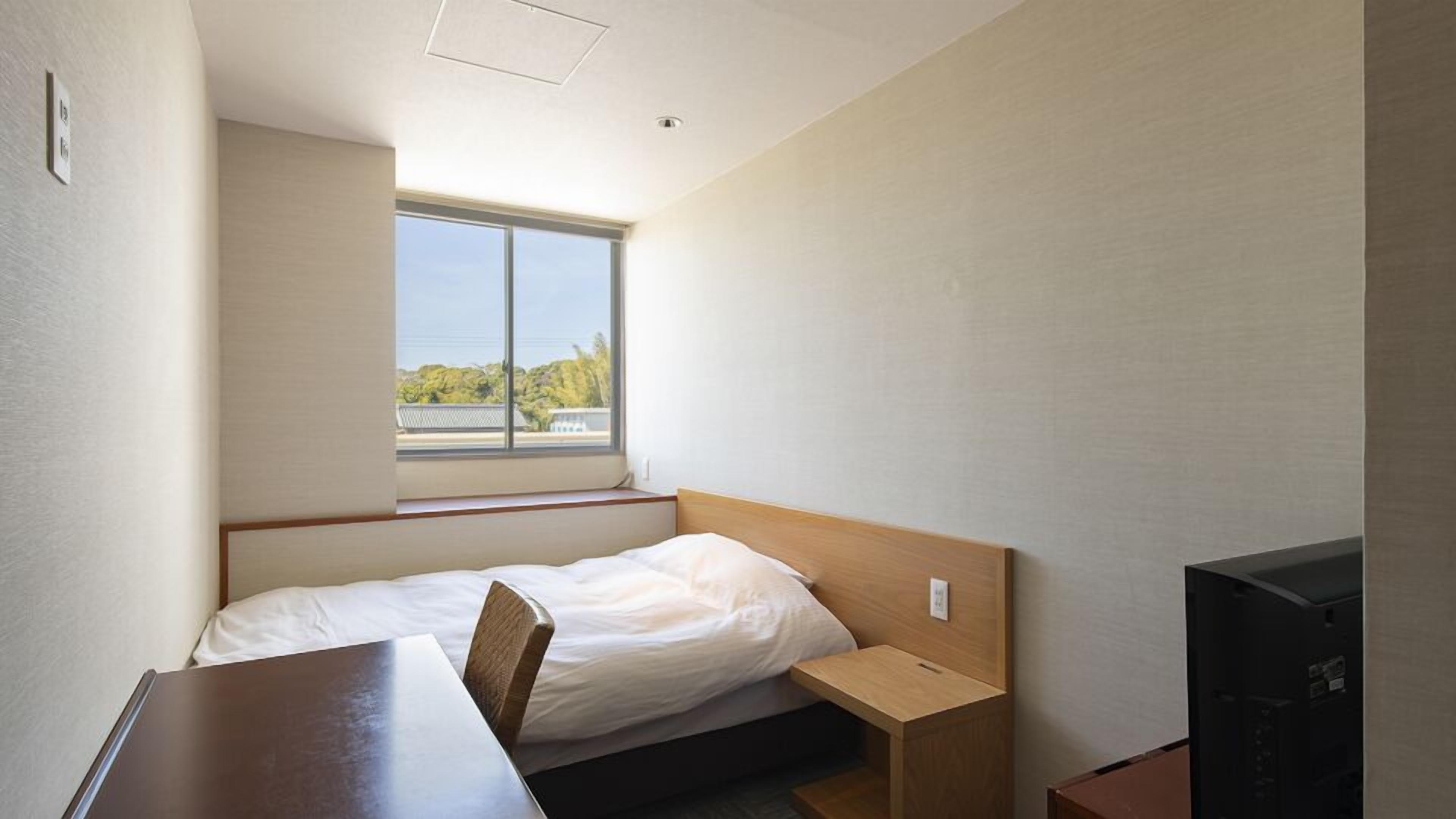 Habitació petita amb un llit individual, una finestra, escriptori i televisió.