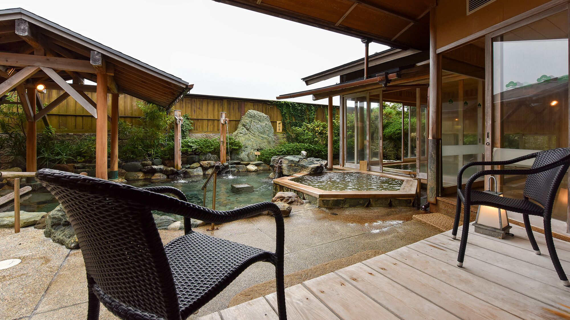 Une terrasse en bois avec des sièges extérieurs, un jardin de rocaille et un espace clos par des parois de verre.
