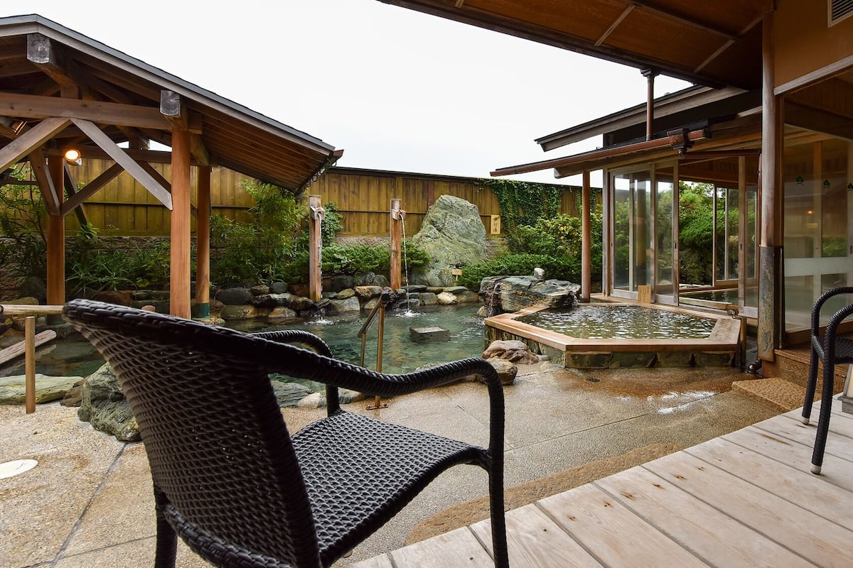Une terrasse en bois avec des sièges extérieurs, un jardin de rocaille et un espace clos par des parois de verre.