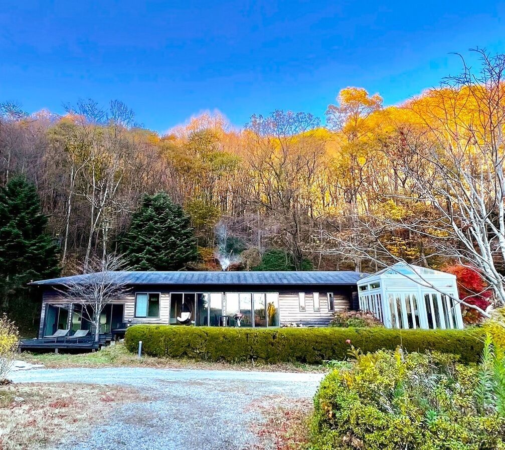 Une maison moderne dotée d’une grande façade vitrée, d’un porche abrité et d’une petite dépendance attenante.