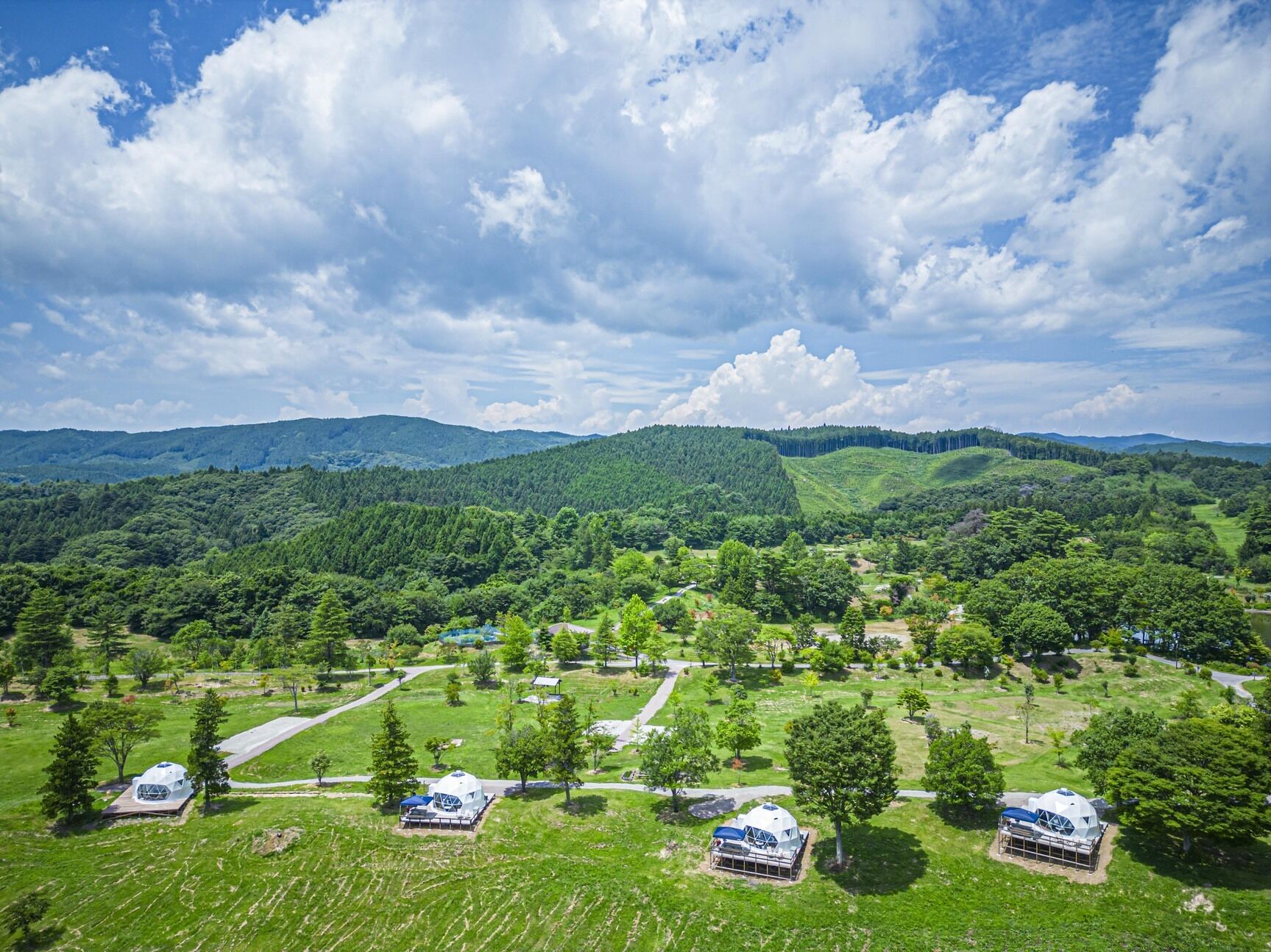 Un paysage composé de plusieurs structures en forme de dôme, entourées de champs verdoyants et d’arbres, sous un ciel partiellement nuageux.
