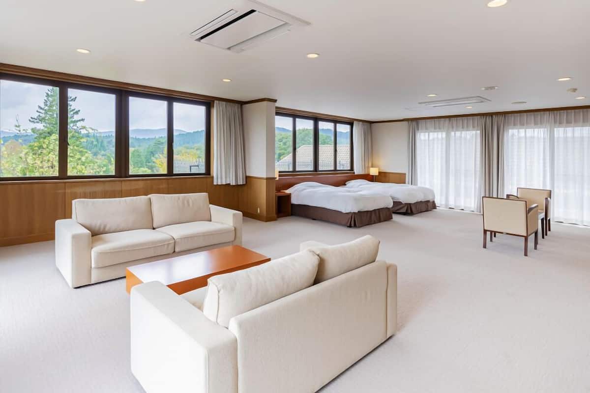 A modern hotel room with a large bed, a sofa, a coffee table, and a desk with chairs.