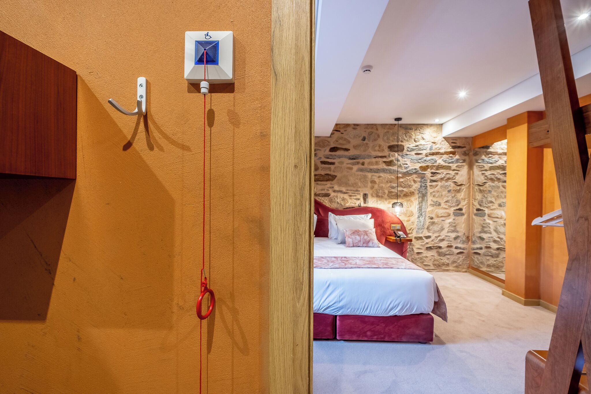 Une chambre avec un mur en pierre, un lit avec une literie rouge et une poutre en bois au plafond.