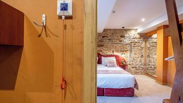 Une chambre avec un mur en pierre, un lit avec une literie rouge et une poutre en bois au plafond.