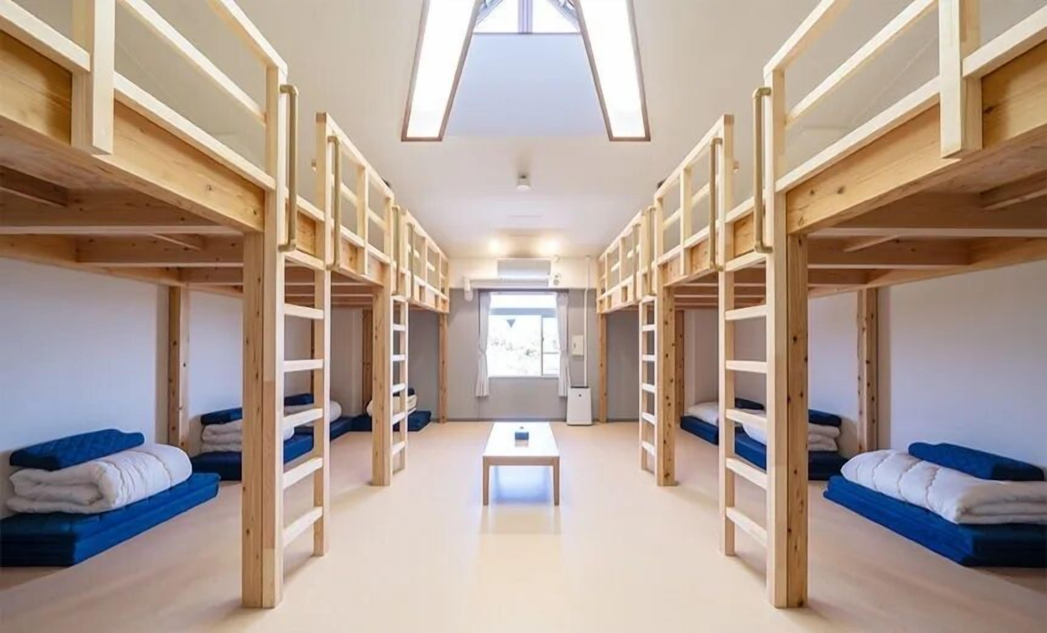 A room with bunk beds and a central table, with a window providing natural light.