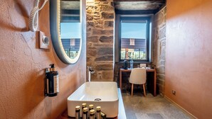 A bathroom with a stone wall, a large mirror, a white sink, and a window. - Cherry Room - Double Superior Room (Paul)