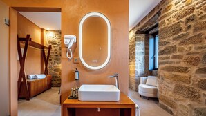 A bathroom with a wooden vanity, a large oval mirror, a hairdryer, and a stone wall. - Cherry Room - Double Superior Room (Paul)