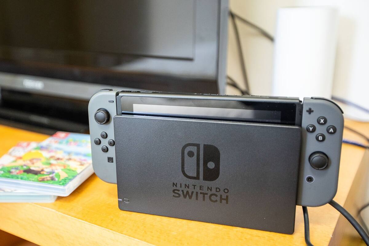 A Nintendo Switch console on a wooden table with a TV in the background.