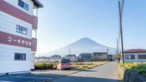 A street view with a building on the left, a parked car in the middle, and a mountain in the background. - Bluebird Hotel (Fujikawaguchiko)