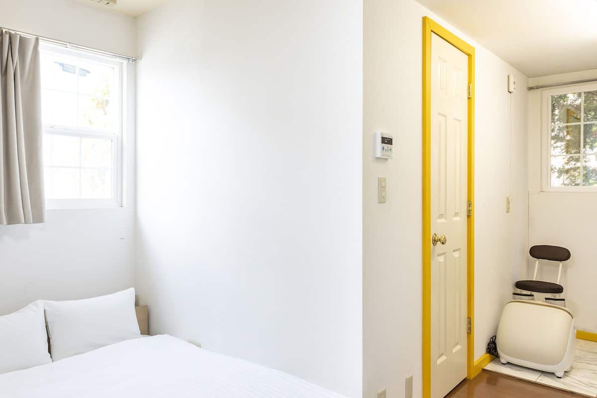 A hotel room with a bed, a window with curtains, a door, and a suitcase.