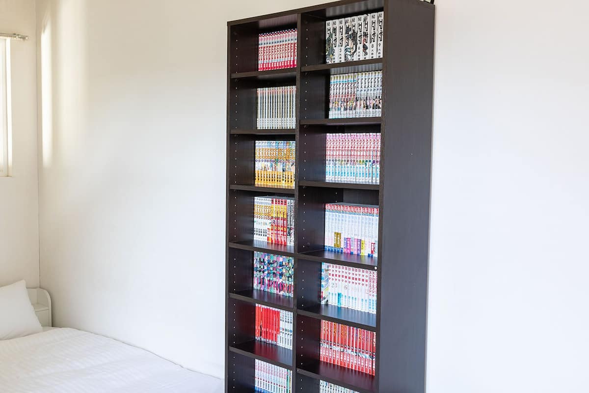 A room with a bed, a window, and a bookshelf filled with books.