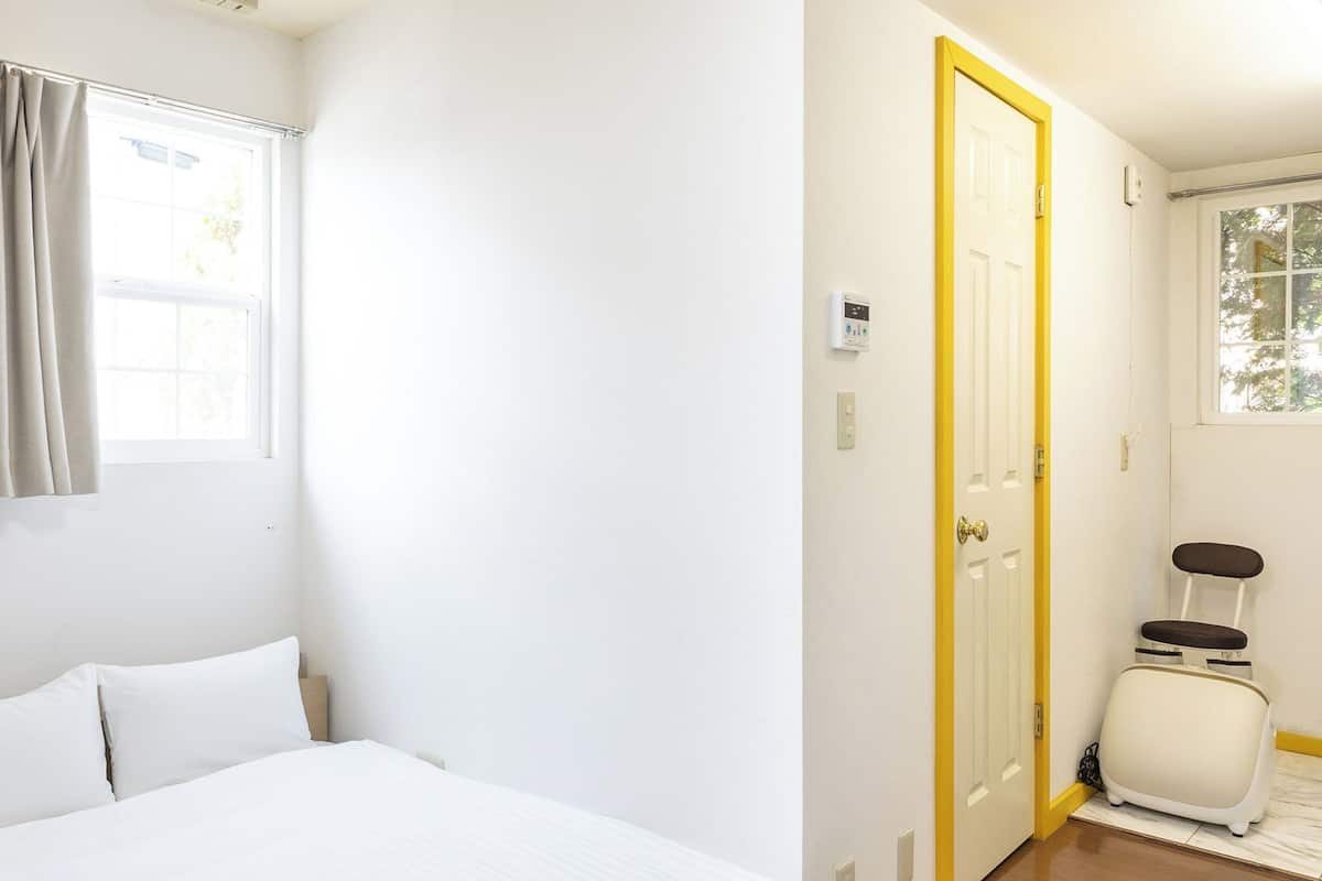 A hotel room with a bed, a window with curtains, a door, and a suitcase.