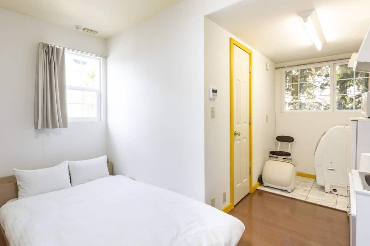 A bedroom with a bed, a window with curtains, a door, a toilet, and a sink.