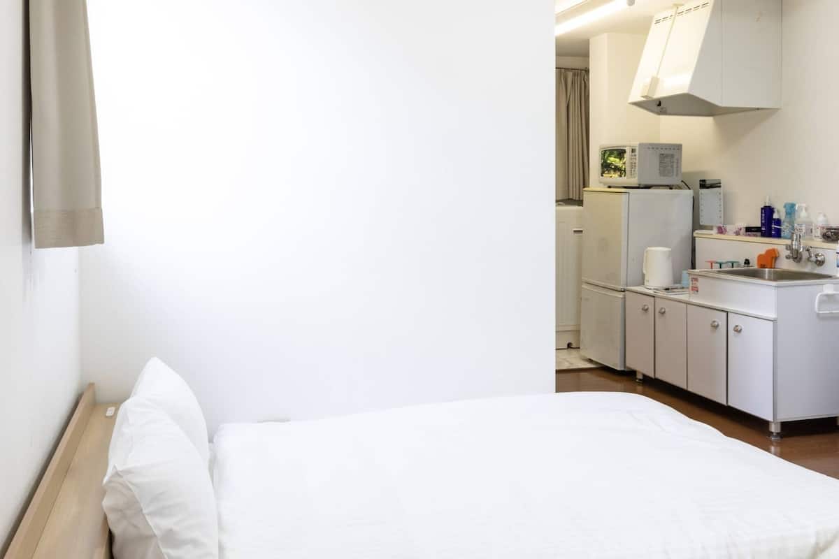 A hotel room with a bed, a small kitchenette, and a bathroom visible through an open door.