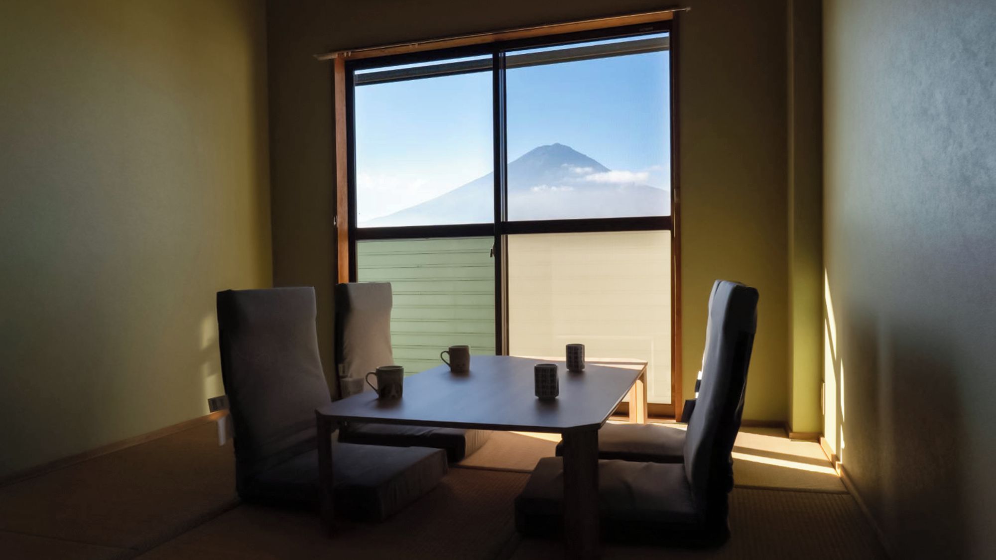 Une pièce avec une table et quatre chaises, une fenêtre donnant sur une montagne et un mur vert.