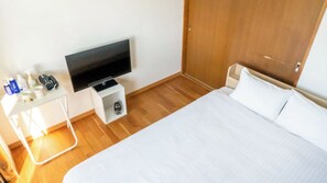 A hotel room with a bed, a television on a stand, a small table with toiletries, and a wooden floor. - Bluebird Hotel (Fujikawaguchiko)