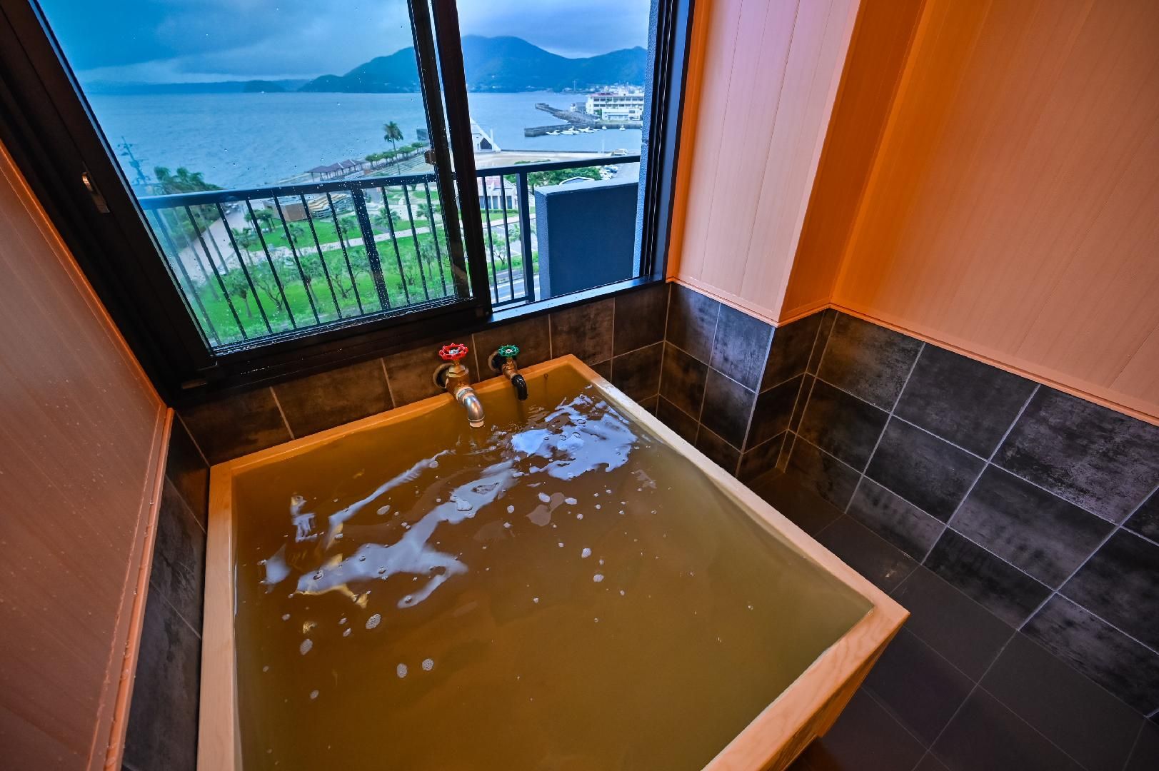 Una bañera con vistas al mar y a las montañas a través de una ventana.
