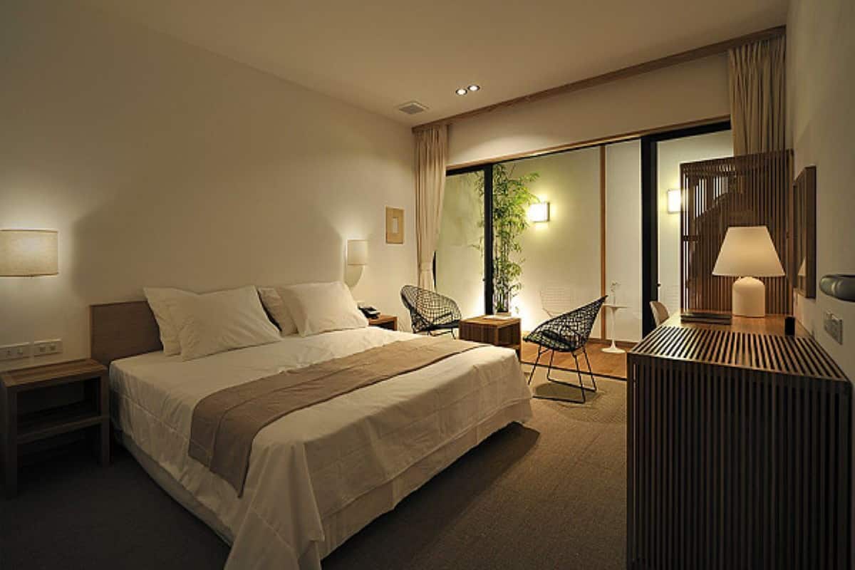 A hotel room with a bed, a chair, a desk, and a lamp.