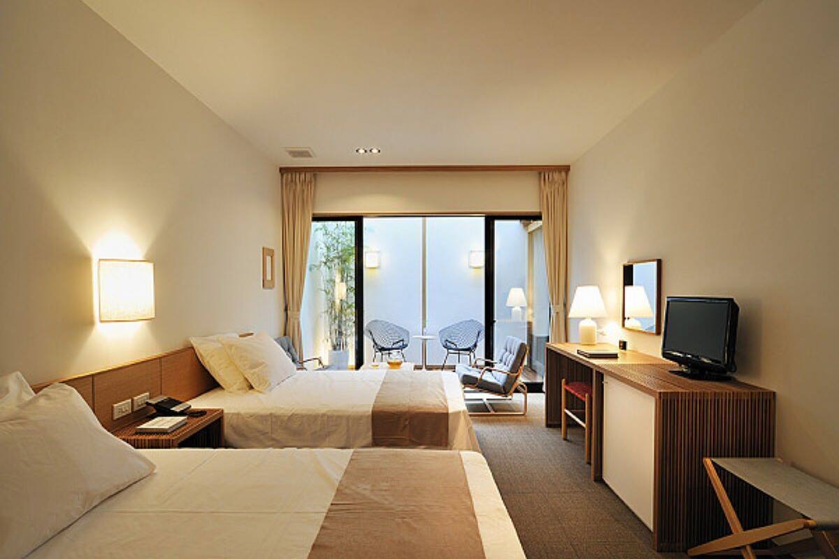 A hotel room with two beds, a desk with a computer, a chair, and a TV.