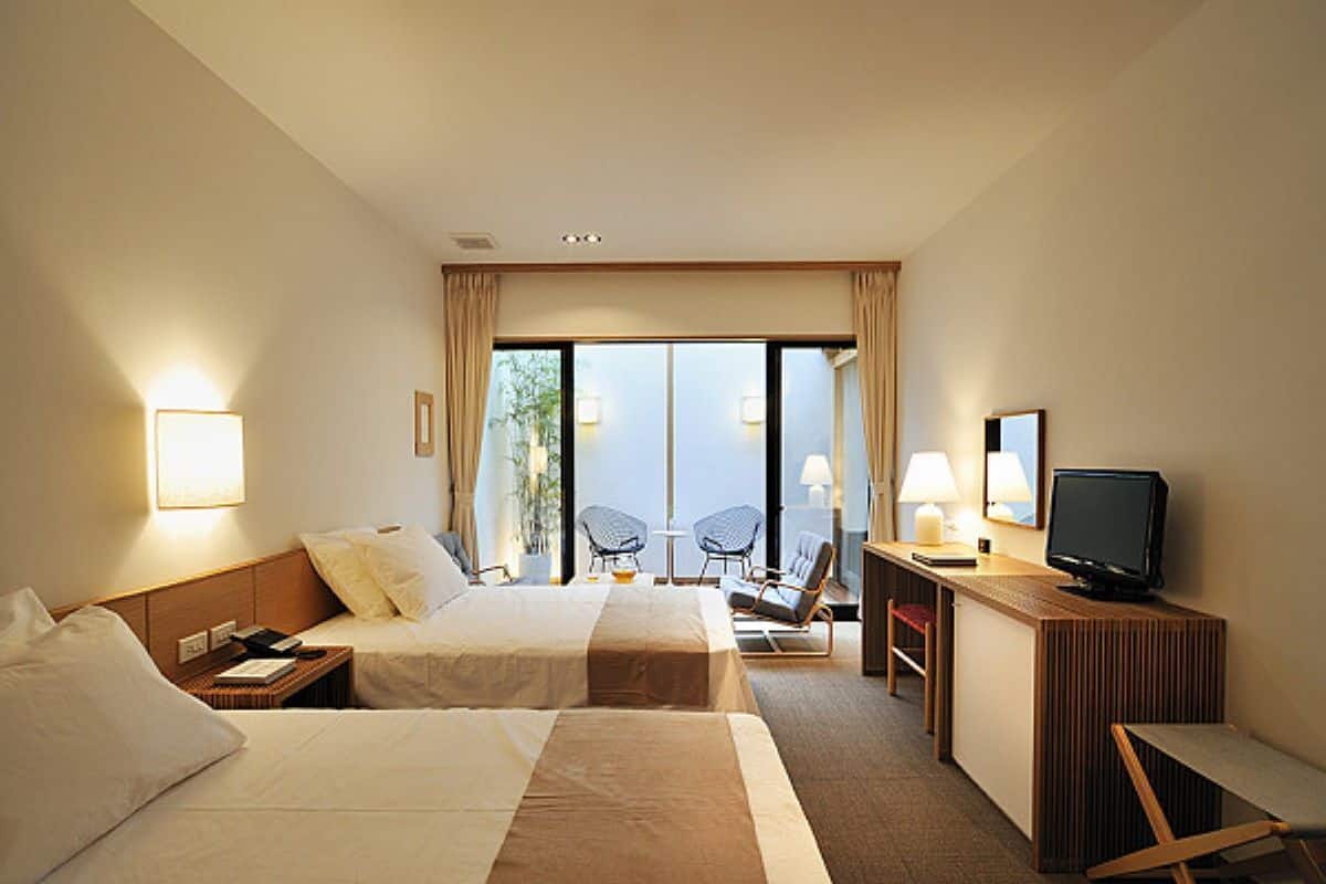 A hotel room with two beds, a desk with a computer, a chair, and a TV.