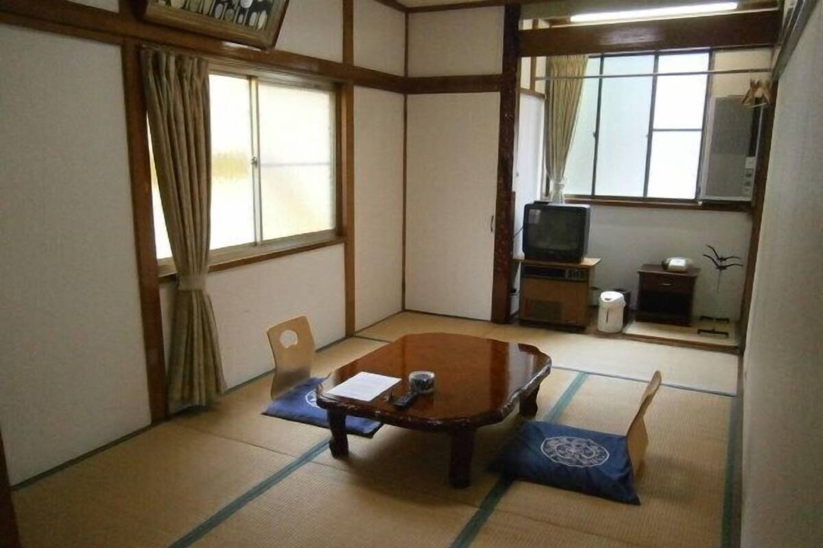 A traditional Japanese room with tatami flooring, a low table, a television, and a small cabinet.