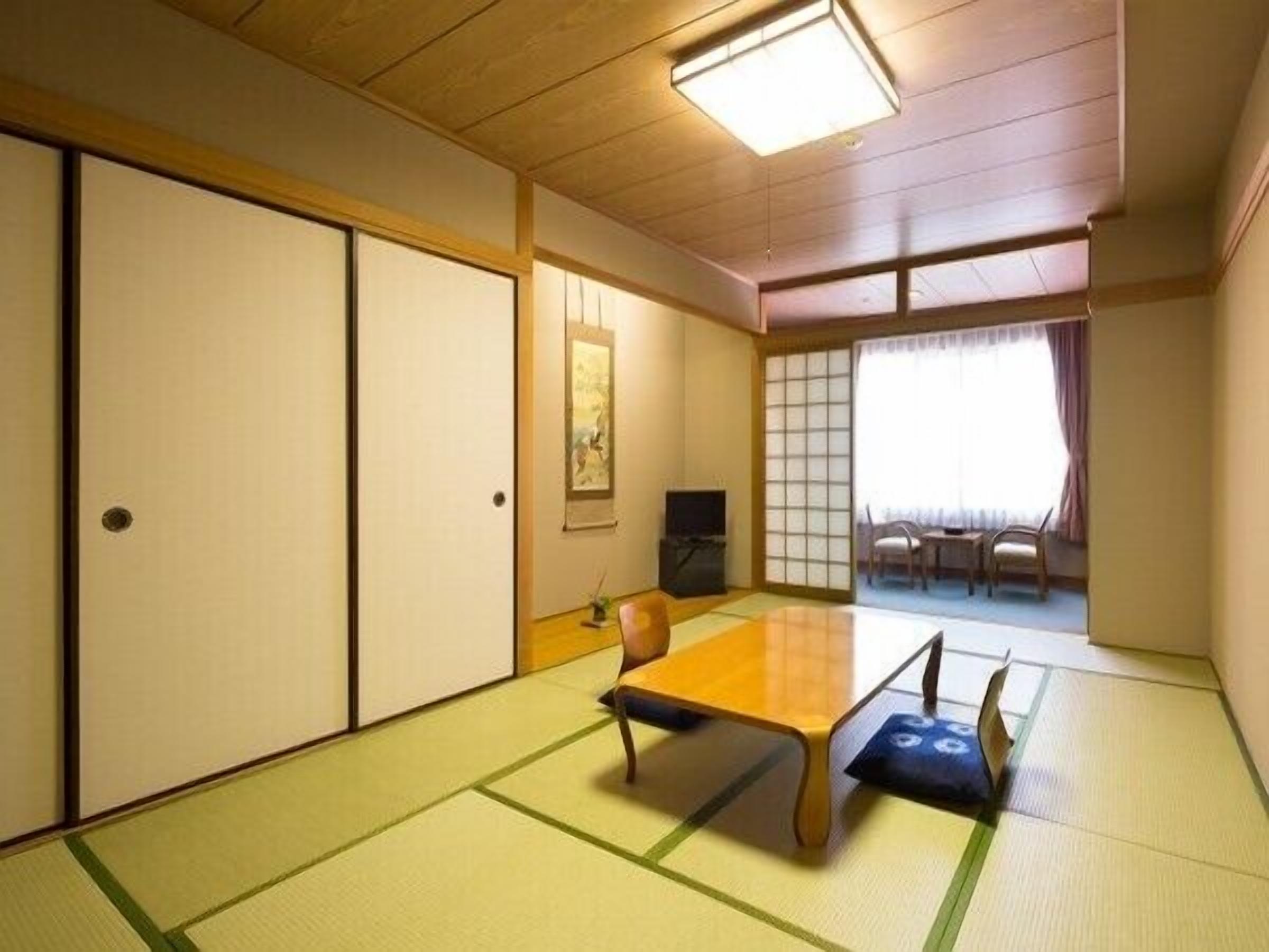A traditional Japanese room with tatami flooring, a low table, sliding doors, and a view through a shoji screen.