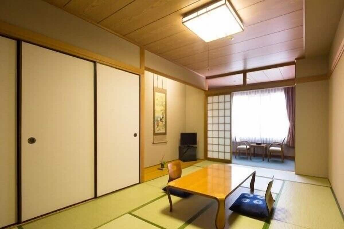 Una habitación tradicional japonesa con suelo de tatami, una mesa baja, puertas correderas y vistas a través de un celosía de papel.