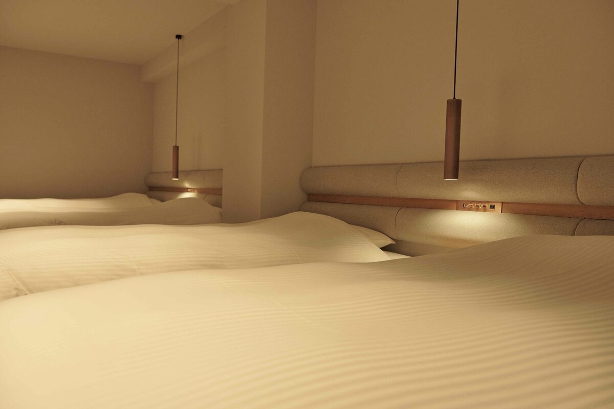 A hotel room with multiple beds, a wooden headboard, and pendant lighting.