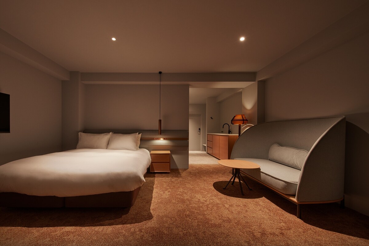 A modern bedroom with a bed, bedside table, and a unique curved sofa.